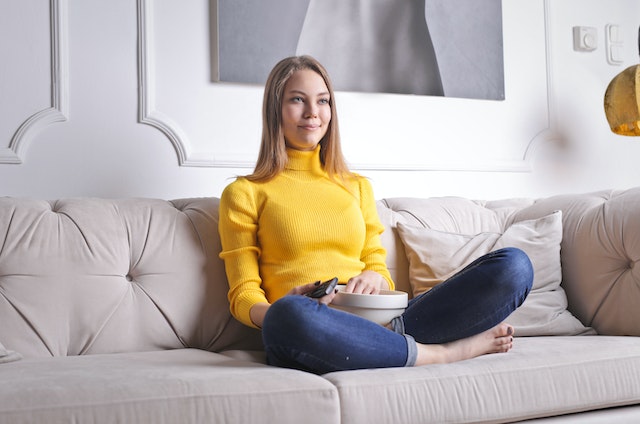 A young woman at home eating popcorn and viewing TV streaming options for the Academy Awards