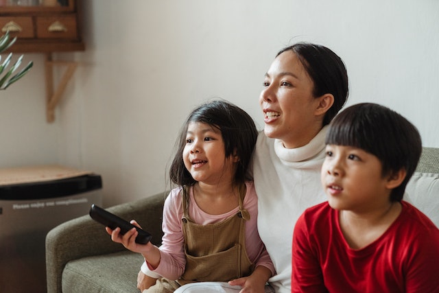 A young boy and girl viewing streaming options for new movies on the couch with their mother