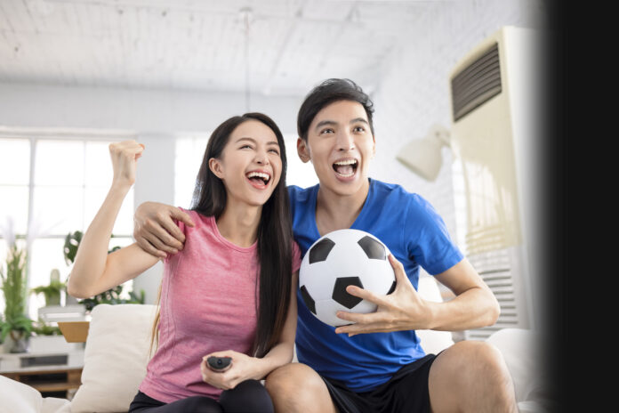 Young couple with soccer ball celebrating while streaming the Women’s World Cup on TV