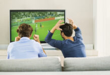 How to Watch the Premier League in 2023 Two men sitting on a couch and reacting while watching a soccer game on TV