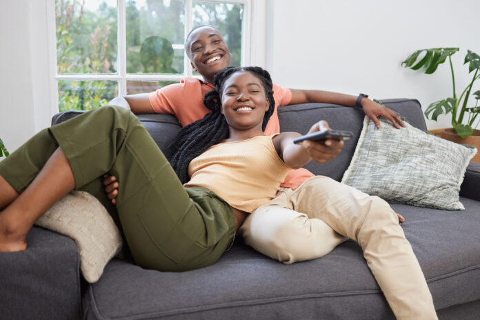 Young couple on the couch searching through streaming services for a new TV show to watch