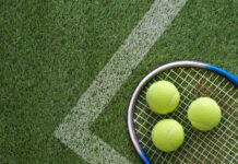 Three tennis balls and a tennis racket lying on a grass tennis court