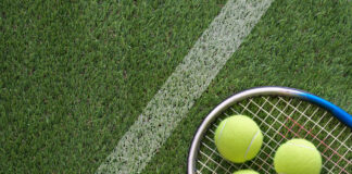 Three tennis balls and a tennis racket lying on a grass tennis court
