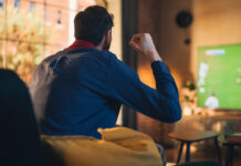 Couple of Soccer Fans Relax on a Couch, Watch a Sports Match at Home in Stylish Loft Apartment. Relaxed young Man and Woman Cheer for Their Favorite Football Club and Enjoying the Weekend.