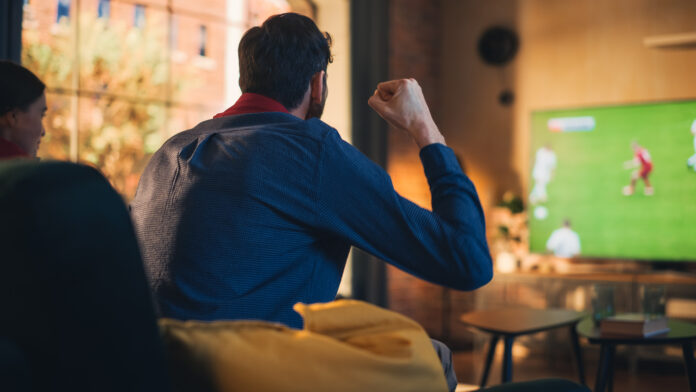 Couple of Soccer Fans Relax on a Couch, Watch a Sports Match at Home in Stylish Loft Apartment. Relaxed young Man and Woman Cheer for Their Favorite Football Club and Enjoying the Weekend.