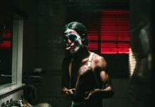 A man in clown makeup smoking a cigarette in the bathroom