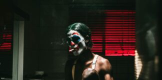 A man in clown makeup smoking a cigarette in the bathroom