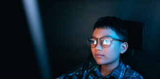 Young kid on the computer playing games, watching entertainment or browsing the online digital internet, wearing glasses and dark background theme.