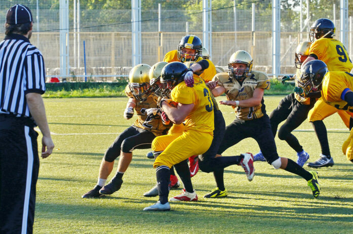 Safely_Watch_NFL_unsplash people playing american football with referee on the field during daytime.