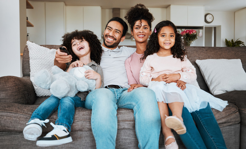 Mom, dad and children on sofa, watching tv and happy family bonding together in living room. Smile, happiness and parents relax with kids on couch, streaming television show subscription or movies.