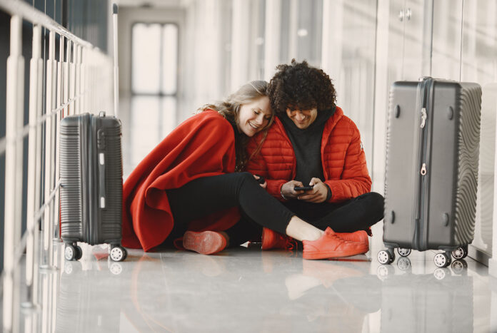 PublicWifi Two happy people in red waiting in airport with luggage sharing wifi on mobile device
