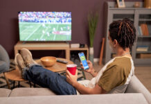 How to Safely Watch the 2026-27 NFL Regular Season Back view at young man watching football game at home and relaxing on couch with mobile streaming