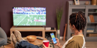How to Safely Watch the 2026-27 NFL Regular Season Back view at young man watching football game at home and relaxing on couch with mobile streaming