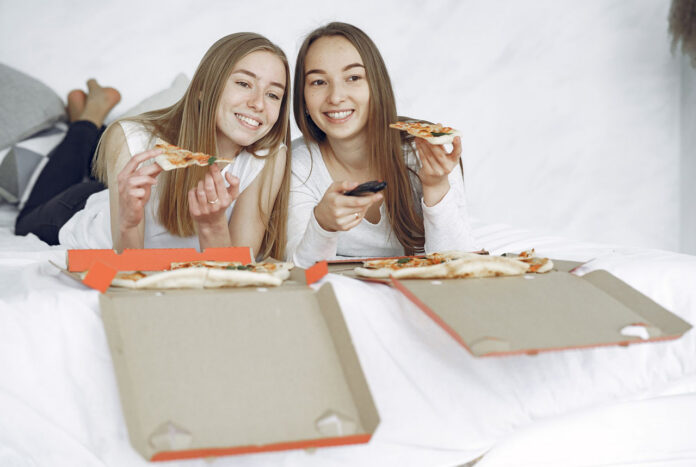 Two happy women with open pizza boxes enjoying a streaming tv movie.