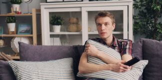 Is It Illegal To Stream Movies and TV Shows Online? What You Need To Know A man sitting on a sofa holding a pillow while watching TV, with a bowl of popcorn beside him.